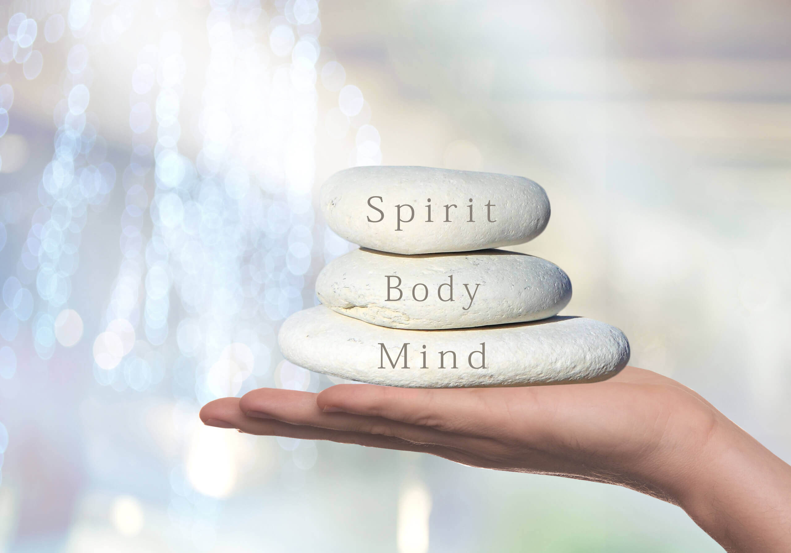 Ausgestreckte Hand hält Steine mit den Aufschriften "Spirit", "Body" und "Mind"