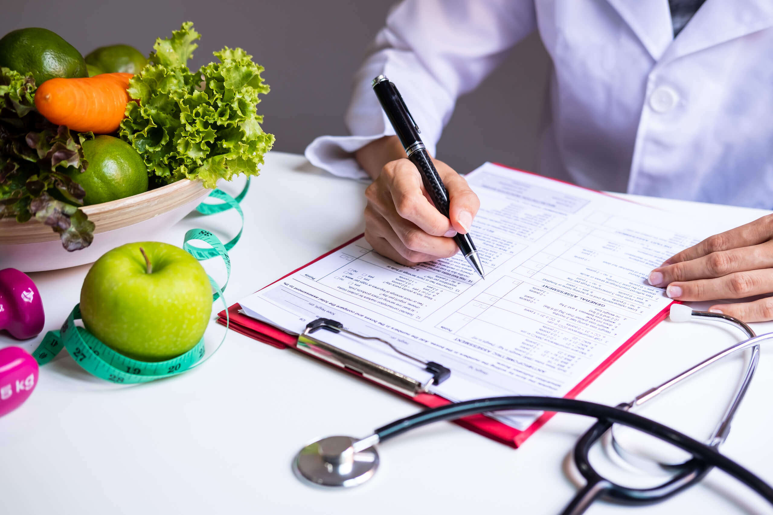 Ärztin beim ausfüllen eines Formulares neben einer Schüssel mit frischem Gemüse und Obst