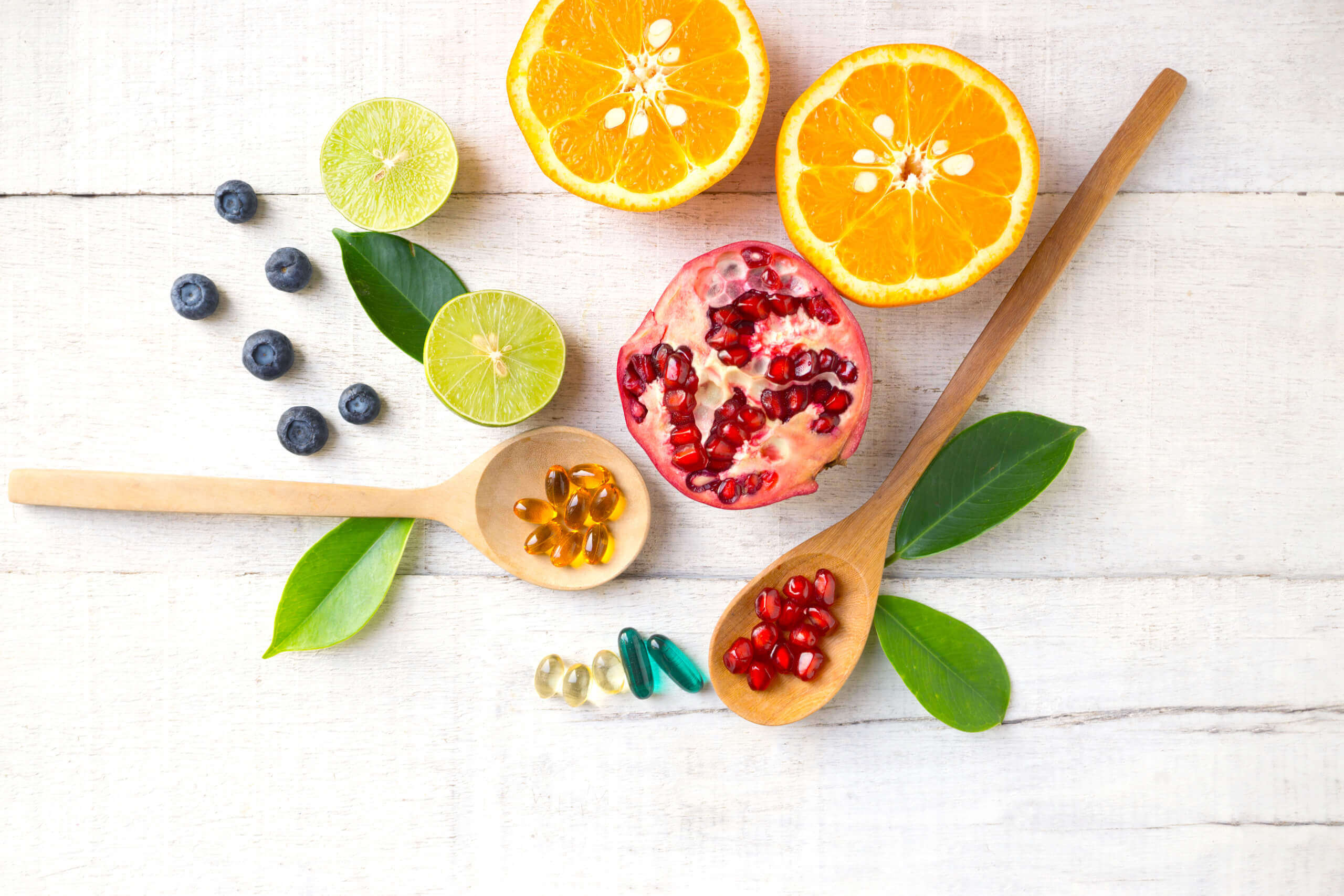 med4you_vitalstofftherapie_00006 Obst und Multivitamin-Supplemente auf Holzlöffeln auf weißem Holzhintergrund